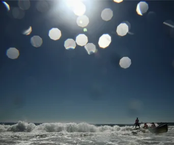 Boat crew navigating waves under a bright sun with lens flare in Newcastle, Australia.