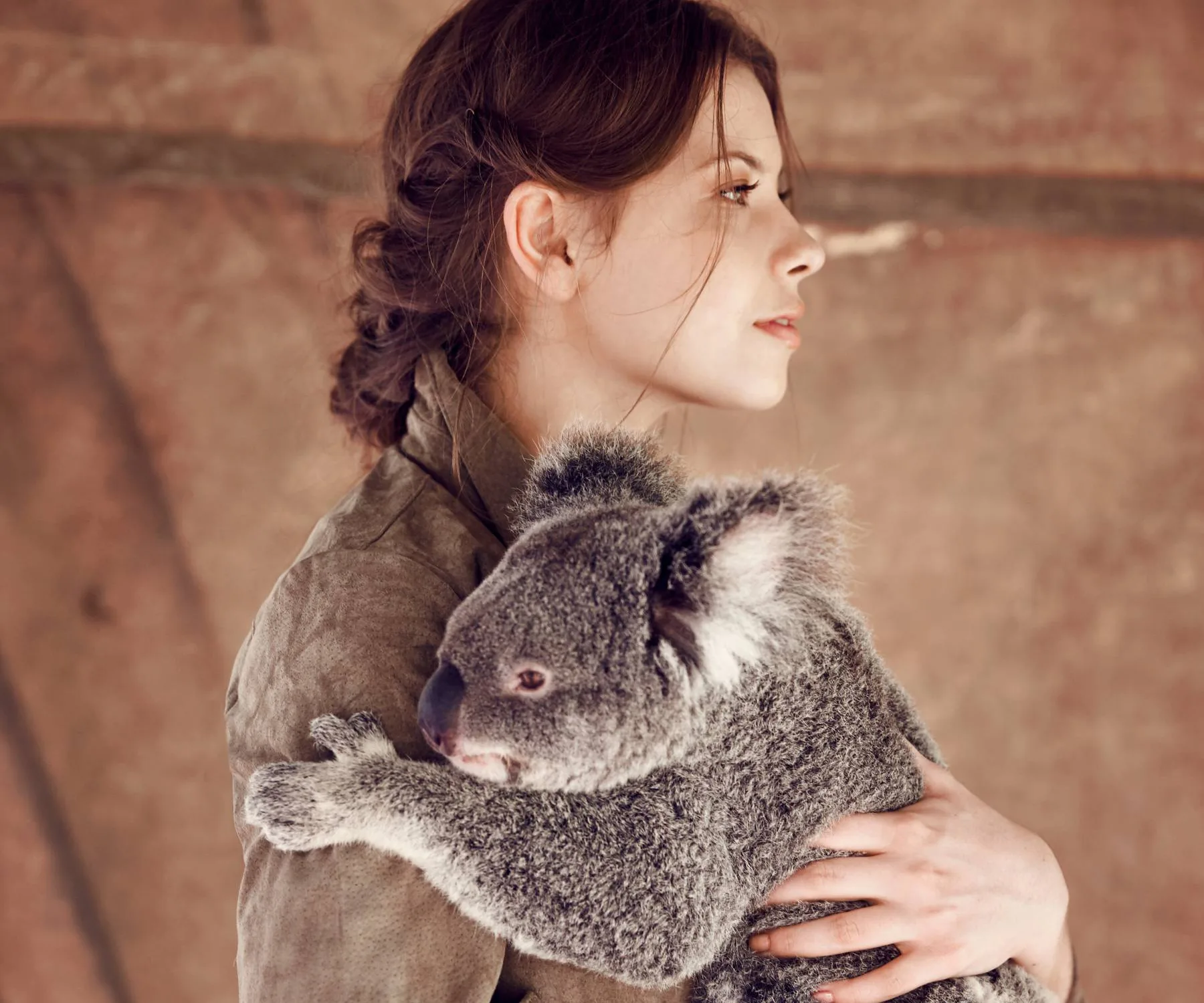 Young woman in profile holding a koala gently against a neutral background.