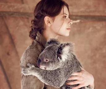 Young woman in profile holding a koala gently against a neutral background.