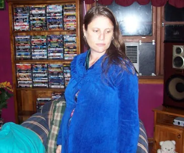 Woman in a blue robe standing in a room with shelves filled with DVDs and a large speaker nearby.