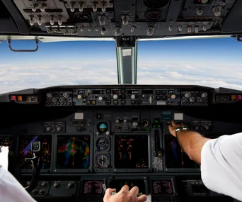 Cockpit view with pilots operating aircraft controls, flying above clouds.
