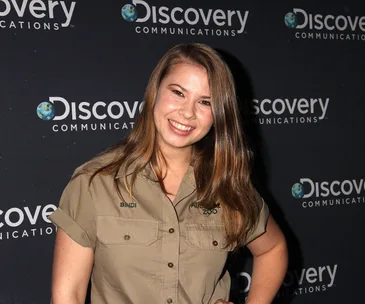 Woman in khaki uniform with "Bindi" name tag smiling at Discovery event backdrop.