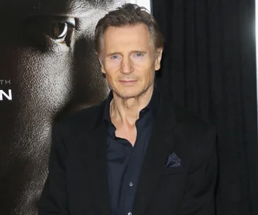 A man in a suit at a movie premiere event. Poster with eye in background.