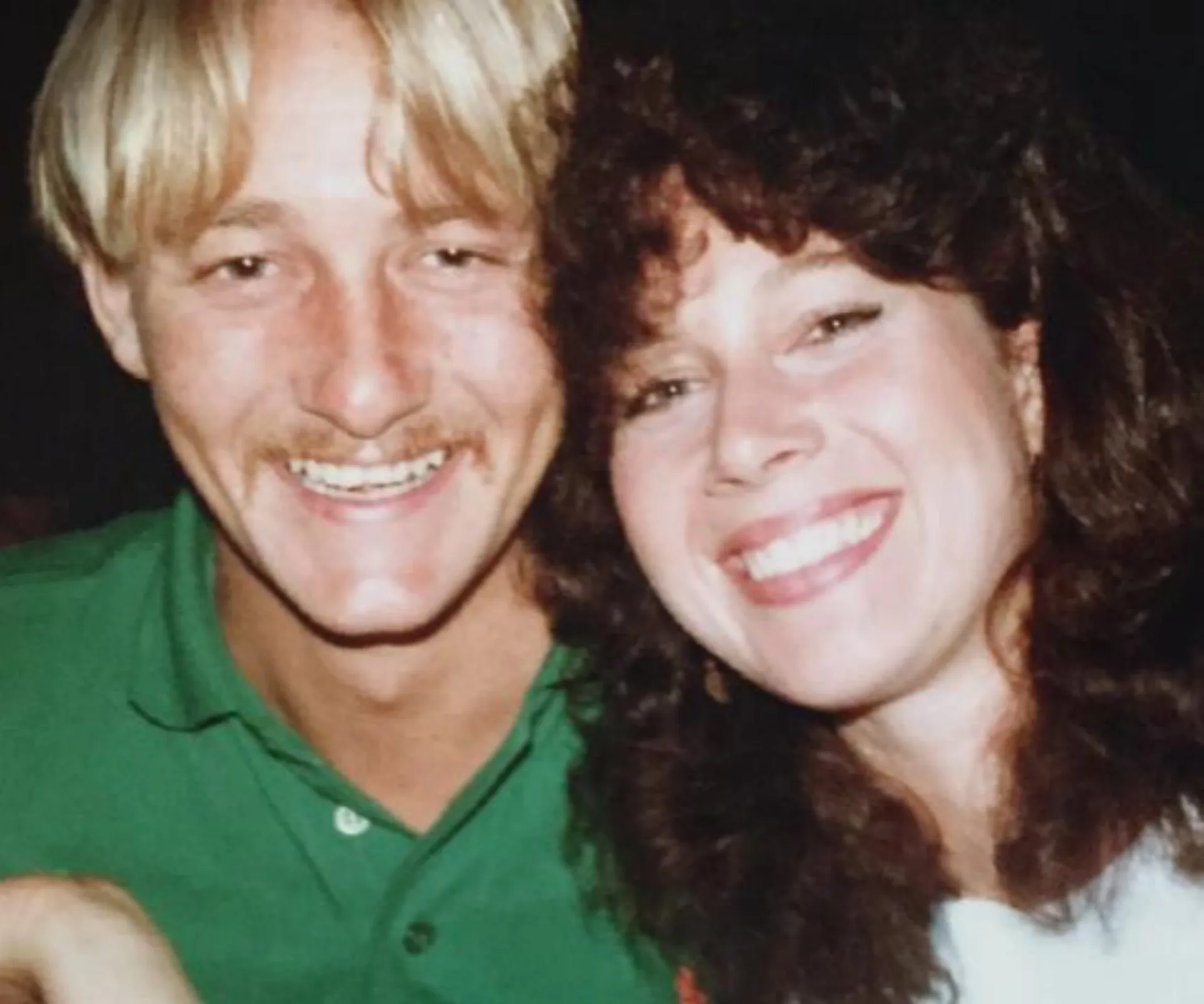 A smiling man in a green shirt and a woman with curly hair pose closely, both appearing happy.