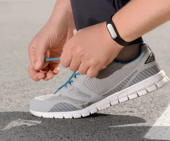 Person tying shoelaces, wearing a fitness tracker, on a sunny day.