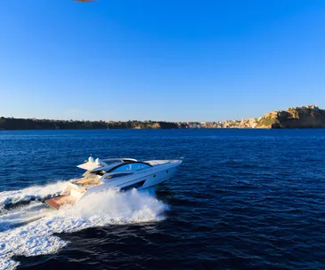 Luxury white yacht cruising in blue ocean near coastal cliffs under clear sky.