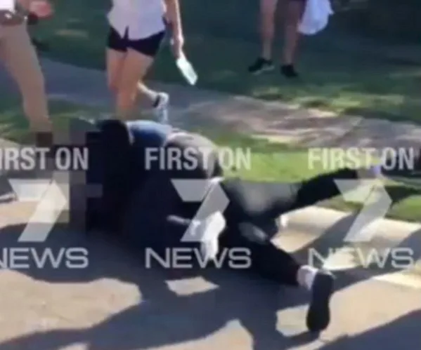 Group of individuals engaged in a physical altercation on a sidewalk, with bystanders observing nearby.