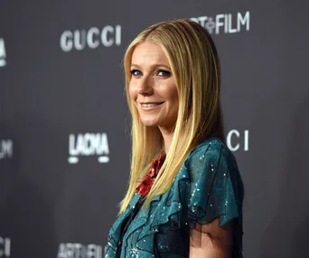 Actress poses on the red carpet at a Gucci event, smiling, in a shimmering blue-green outfit.