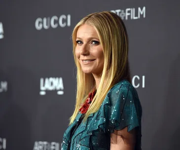 Actress poses on the red carpet at a Gucci event, smiling, in a shimmering blue-green outfit.