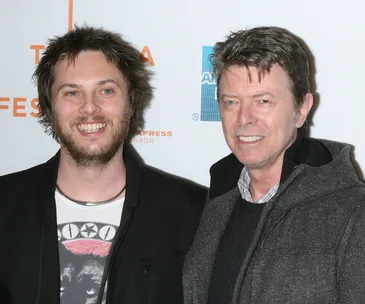 Two men smiling at a film festival, one with short spiky hair and a beard, the other with short hair, wearing a jacket.