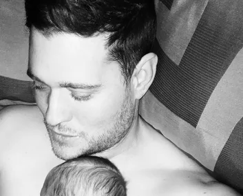 A man lovingly looks at a baby resting on his chest, both in a close and tender embrace.