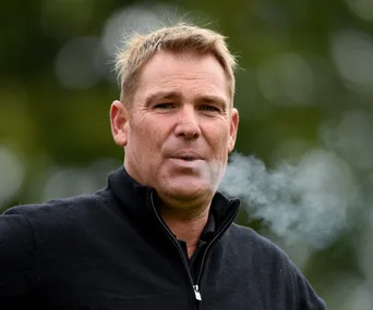 Man in a black jacket outdoors, exhaling smoke.