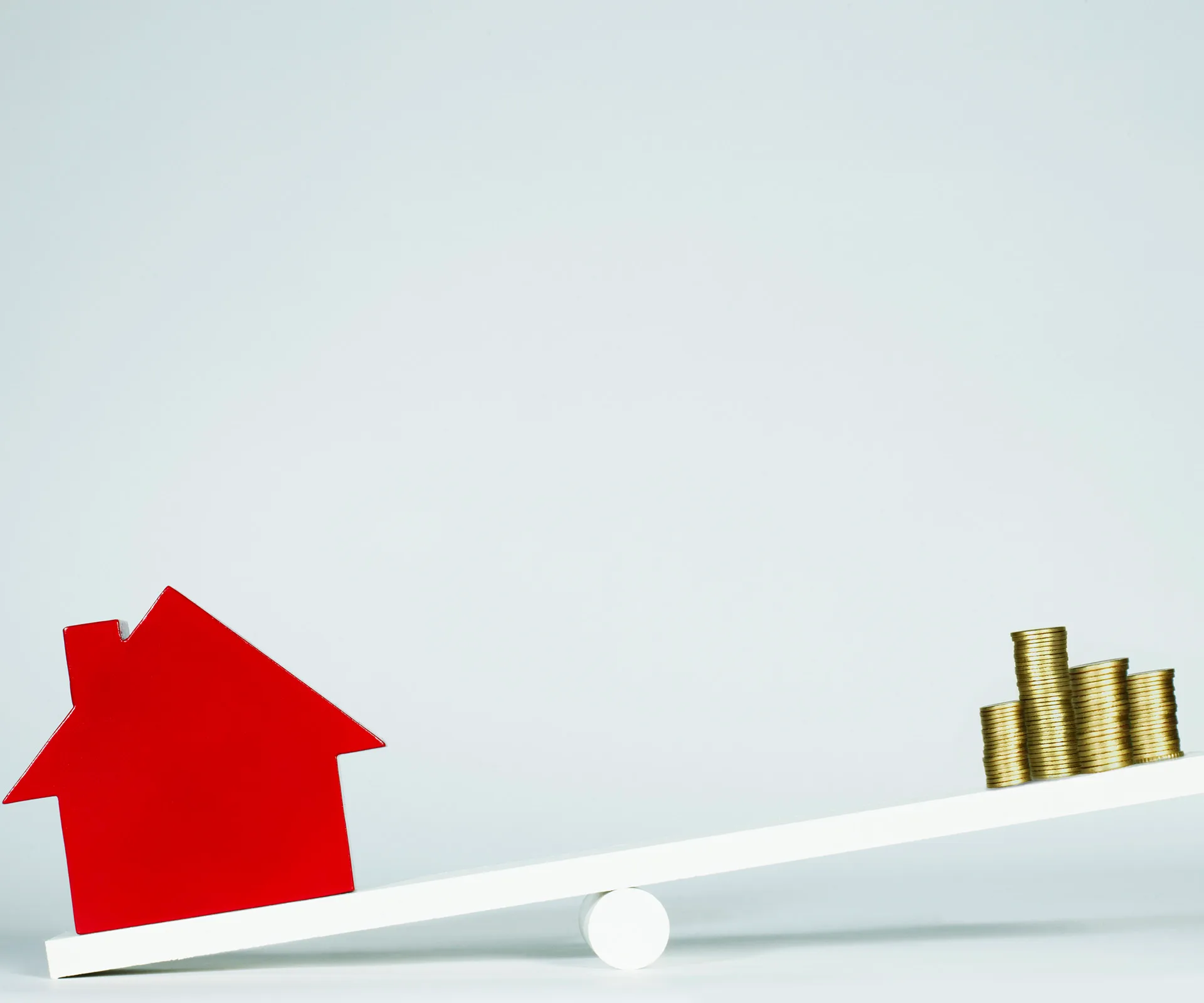 Seesaw with red house model on one end and stack of coins on the other, balancing concepts of property and investment.
