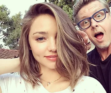 Miranda Kerr with short hair, smiling with a man making a surprised expression in the background.