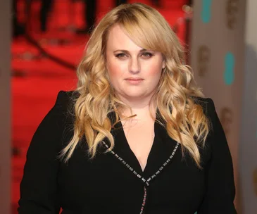 A person with long blond hair in a black outfit on a red carpet at a formal event.