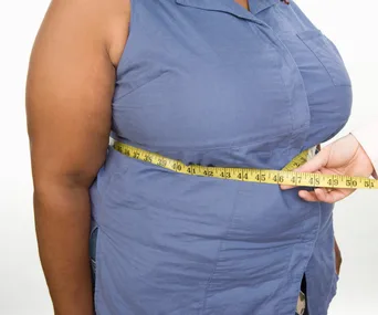 A person in a blue shirt has their waist measured with a yellow tape measure.