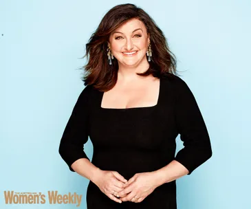 Woman smiling in a black dress against a light blue background; "The Australian Women's Weekly" logo in corner.