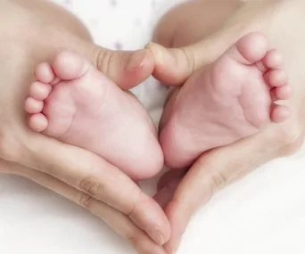 Baby feet cradled in a person's hands, forming a heart shape.