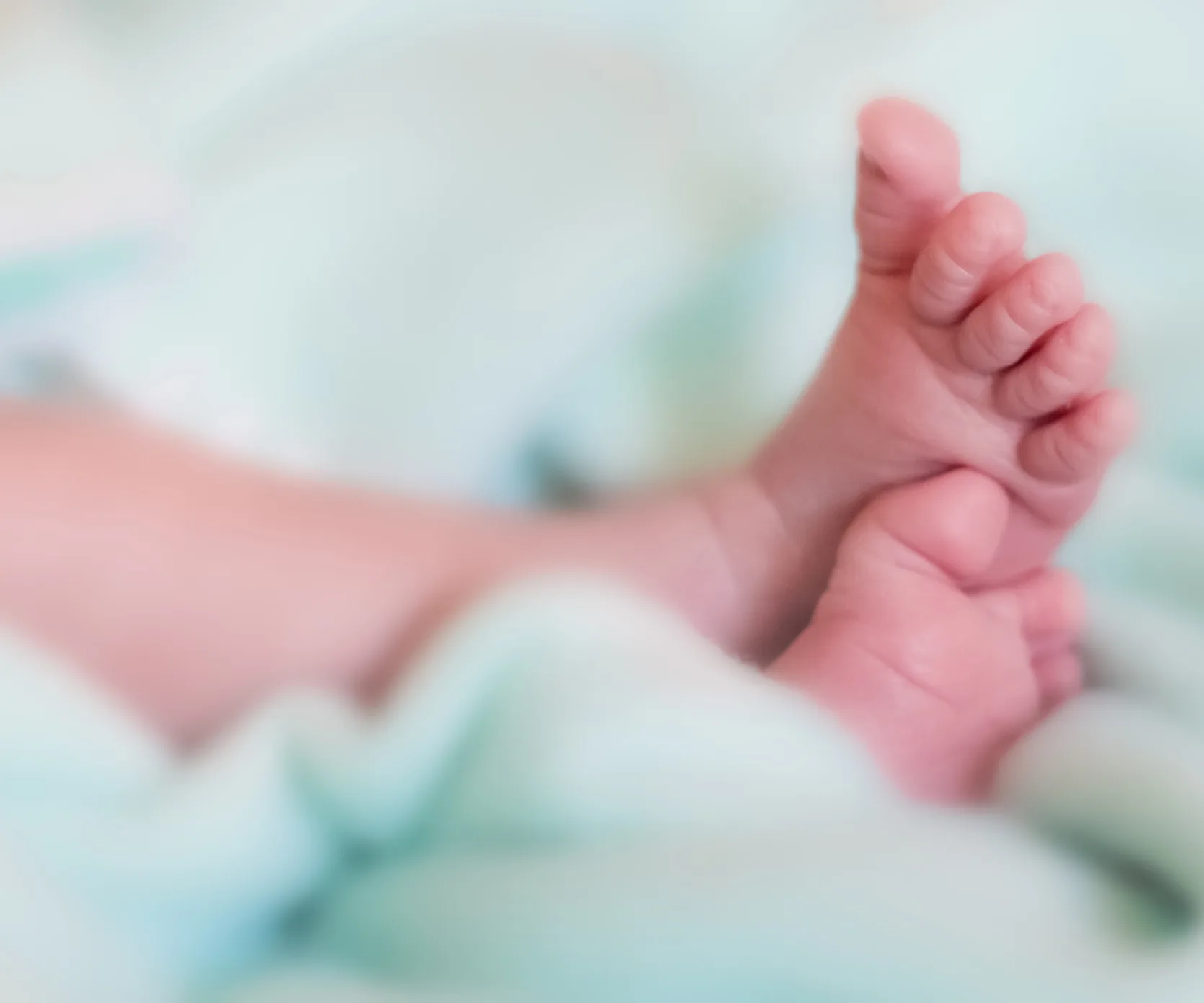 "Close-up of baby feet wrapped in a soft, light green blanket, creating a serene and tender atmosphere."