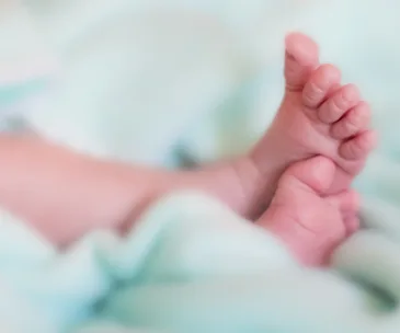 "Close-up of baby feet wrapped in a soft, light green blanket, creating a serene and tender atmosphere."