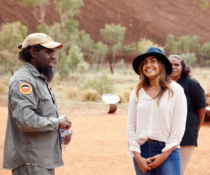 Jessica Mauboy smiling in conversation with two individuals at Uluru.