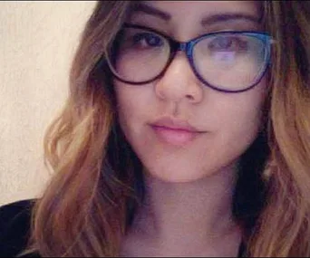 A woman with long hair and glasses looks at the camera with a neutral expression.