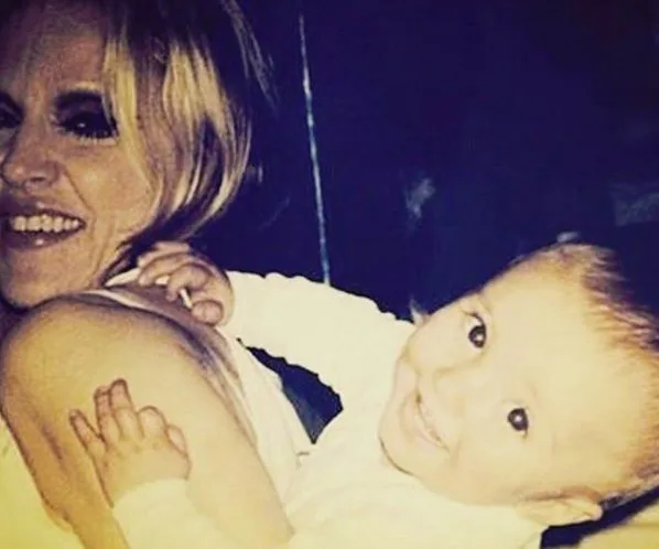 Woman smiling while holding a smiling baby, both looking at the camera.