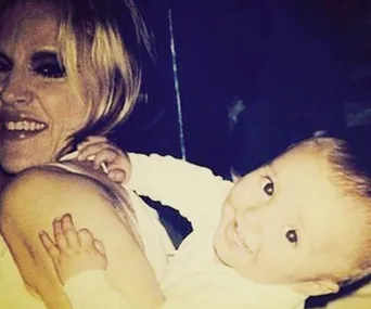 Woman smiling while holding a smiling baby, both looking at the camera.