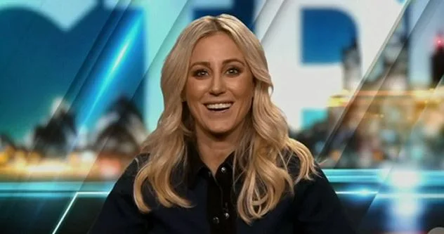 A woman with long blonde hair smiling at a camera, sitting against a blurred, illuminated geometric background.
