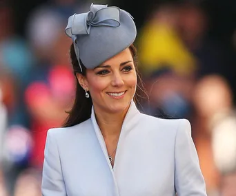 I don't know who this person is, but they are wearing a light blue outfit and hat, smiling in a blurred crowd background.