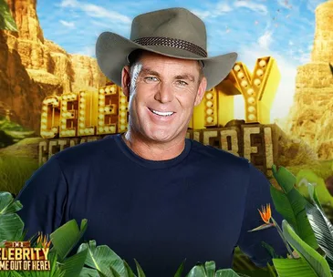 Australian man in a wide-brimmed hat, smiling, with "I'm a Celebrity" backdrop, amidst lush jungle scenery.
