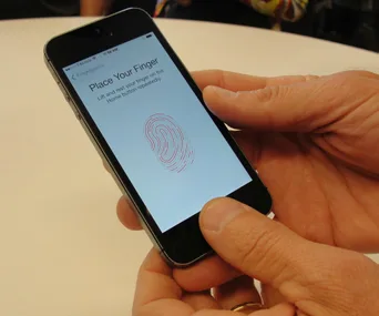 Person holding an iPhone with fingerprint scanning instructions displayed on the screen.
