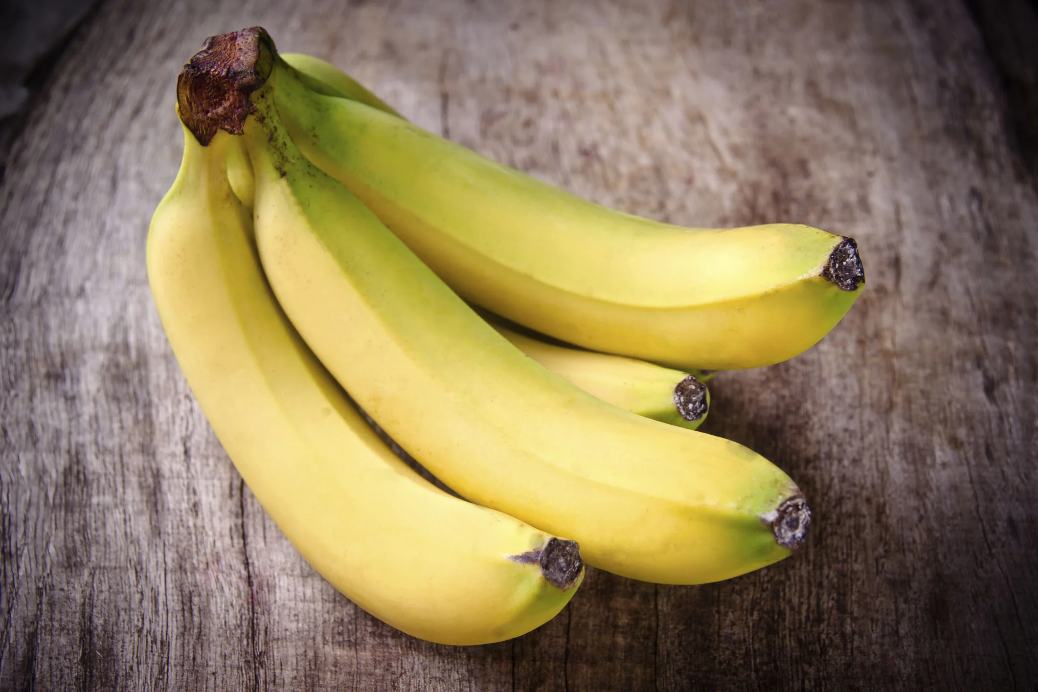 A bunch of ripe yellow bananas on a wooden surface.