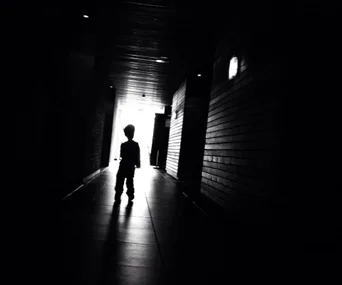 Silhouette of a child standing in a dark corridor with light shining at the end.