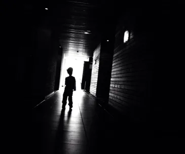 Silhouette of a child standing in a dark corridor with light shining at the end.