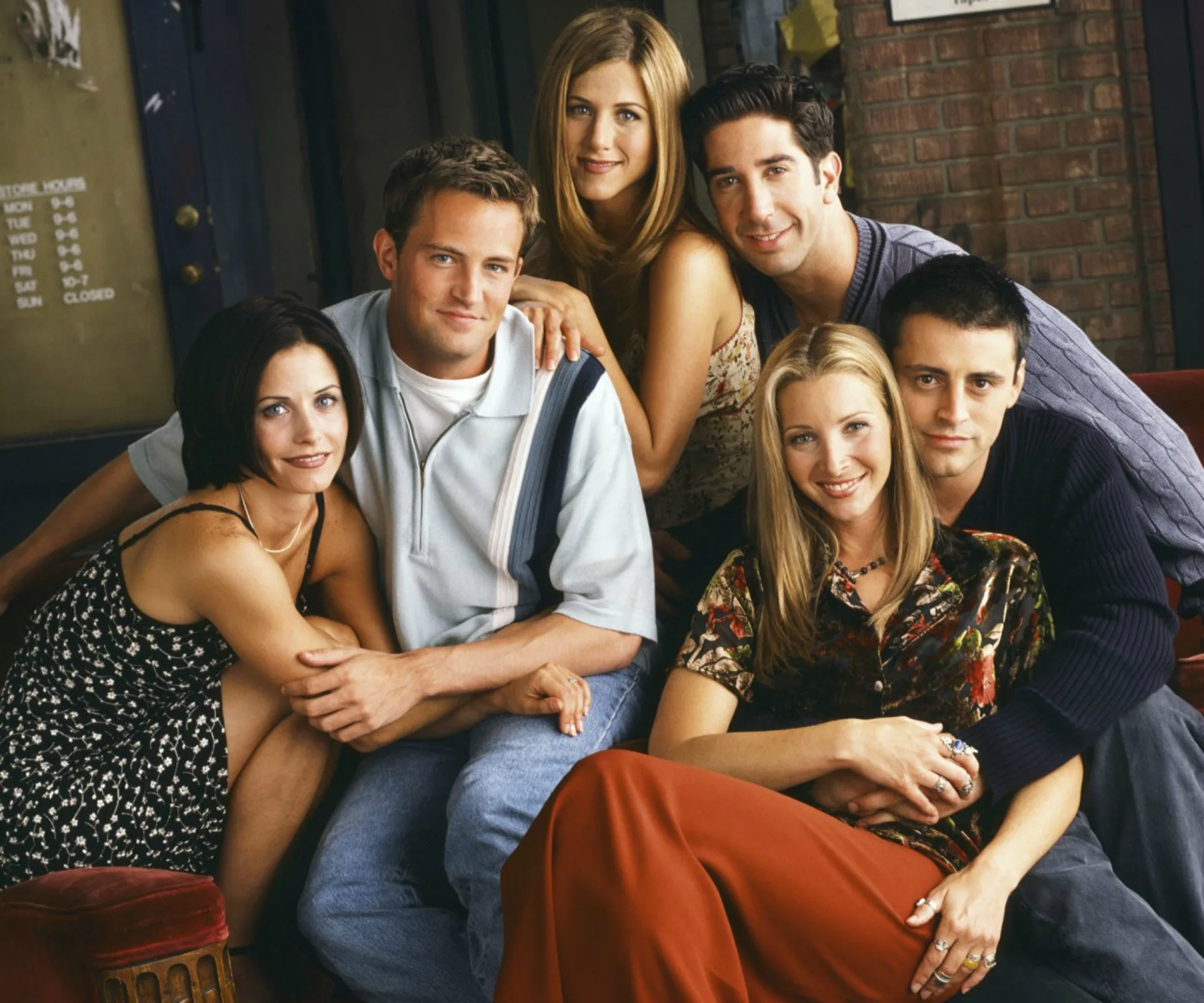 A group photo of the six main cast members of "Friends" sitting together in a cozy setting.