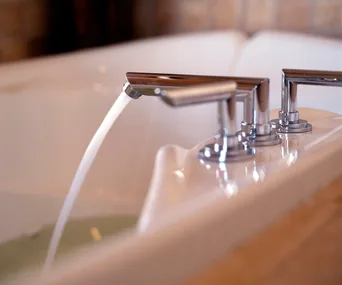 Close-up of a modern bathtub faucet with water flowing into the tub.