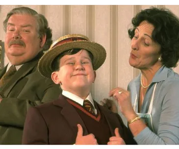 A young boy in a straw hat and brown blazer poses confidently between a proud older man and a smiling woman.