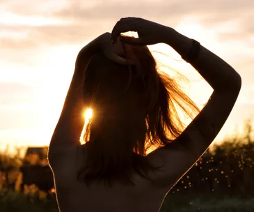 Silhouette of a person with hands in hair, backlit by the sunset, creating a glowing effect around them.