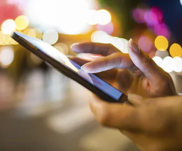 Hands using a smartphone with a blurred urban background at night.