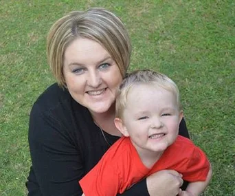 Mother and young son smiling while sitting on grass.