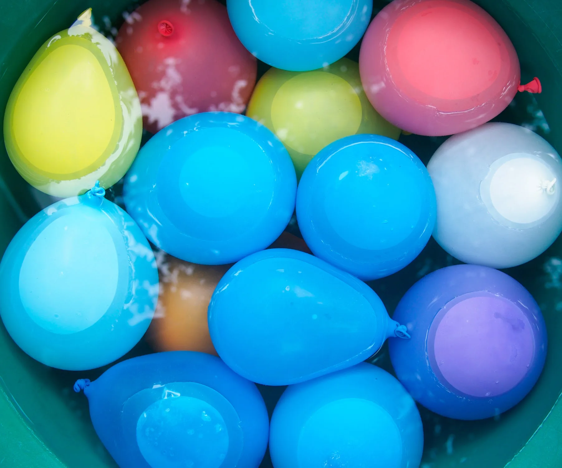 Colorful water balloons floating in a green tub filled with water.