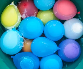 Colorful water balloons floating in a green tub filled with water.