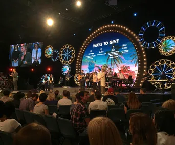 Hillsong service with a band performing on stage, audience seated, and a large screen displaying "Ways to Give".