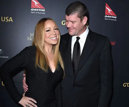 Mariah Carey in a black dress smiling beside a man in a suit, posing on a red carpet event.