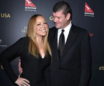 Mariah Carey in a black dress smiling beside a man in a suit, posing on a red carpet event.