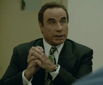 I don’t know who this person is, but they appear to be wearing a suit and tie, seated with hands clasped.