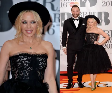 Singer in a black lace dress and hat poses with a man in a suit at the 2016 Brit Awards red carpet.