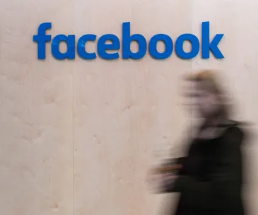 A blurred person walking past a wall with the Facebook logo in blue.