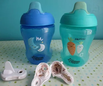 Two Tommee Tippee sippy cups with moldy valves on a polka dot surface.